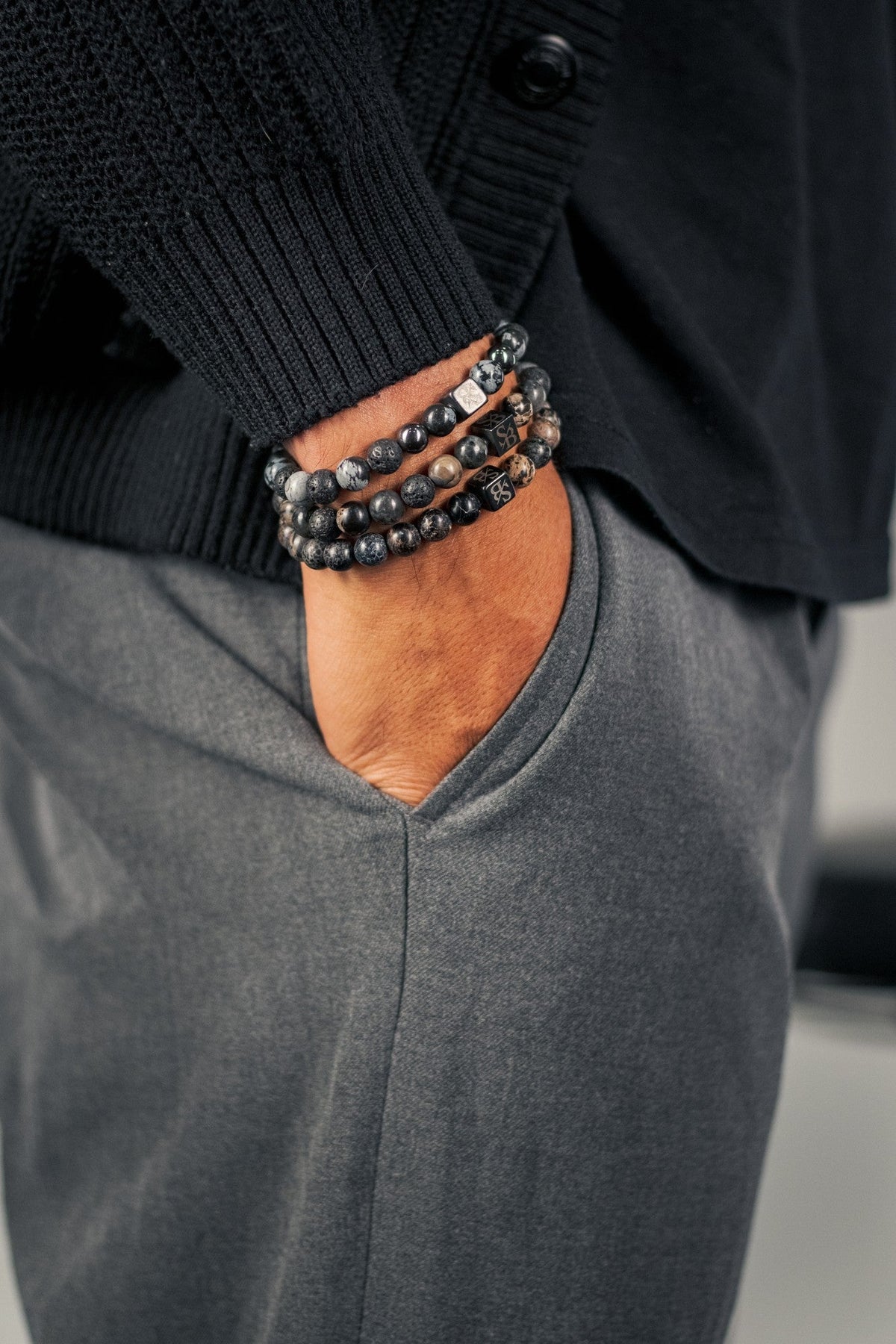 Drie donkere natuurstenen armbanden met zilveren accentkralen aan een mannenpols
