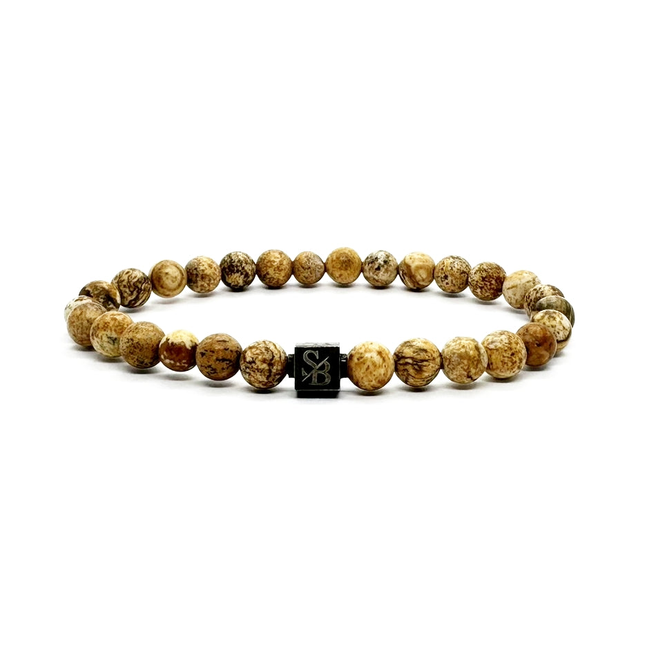 Een Stoney Bracelets Matte Desert Jaspis Stones (6mm) armband met ronde, lichtbruin gemarmerde kralen en een centrale zwarte vierkante "SB"-gegraveerde kraal, afgebeeld op een witte achtergrond.