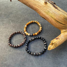 Drie Afrikaanse stenen (8 mm) armbanden met tijgeroogkralen bovenop een boomstam van Stoney Bracelets.