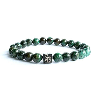 Een groene kralenarmband, bestaande uit een mix van donkere en lichte 8 mm donkere Afrikaanse turquoise stenen van Stoney Bracelets, met een zilveren vierkante bedel met de tekst "SB" erop, afgebeeld op een witte achtergrond.