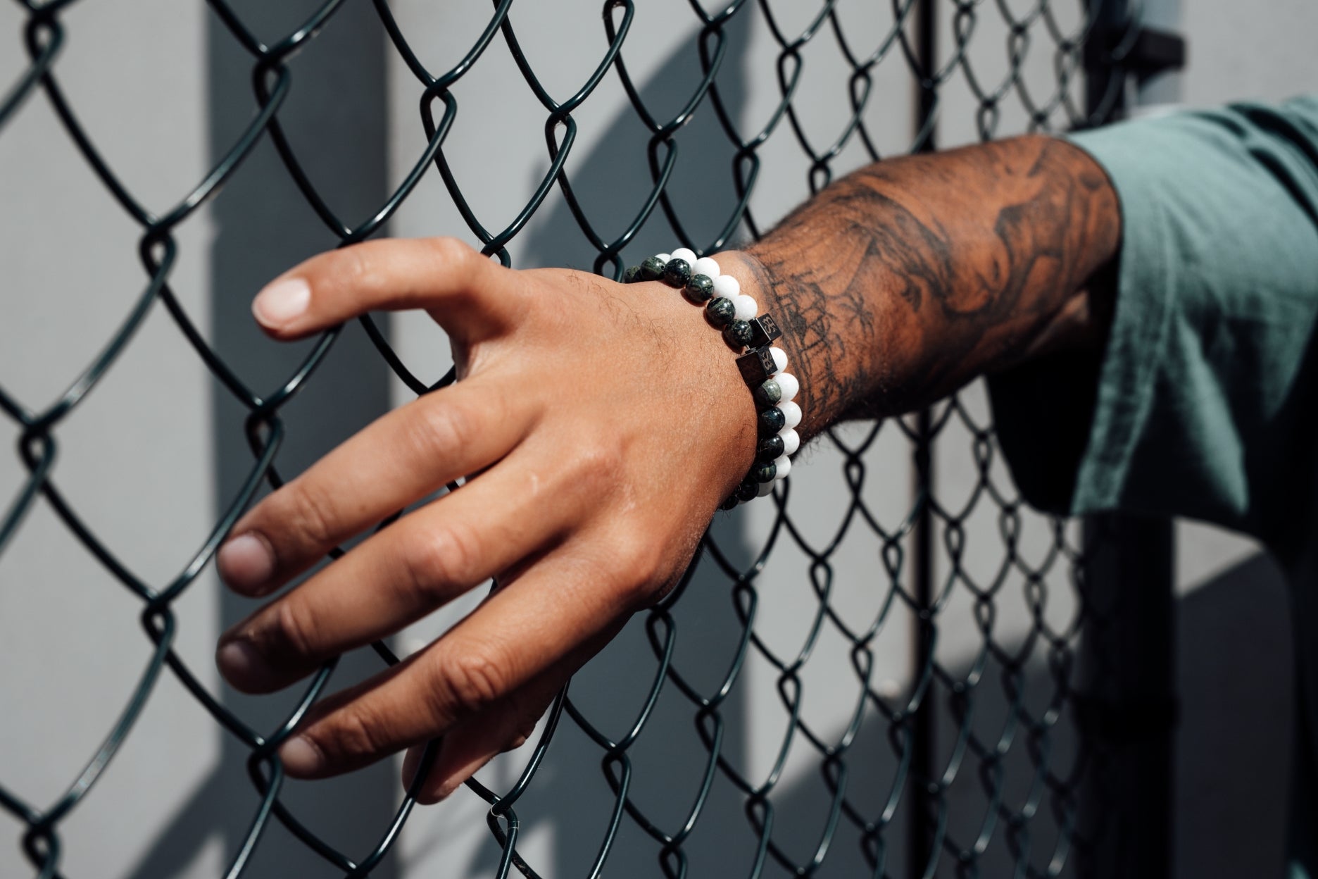 Een man met tatoeages die een armband tegen een hek houdt.
