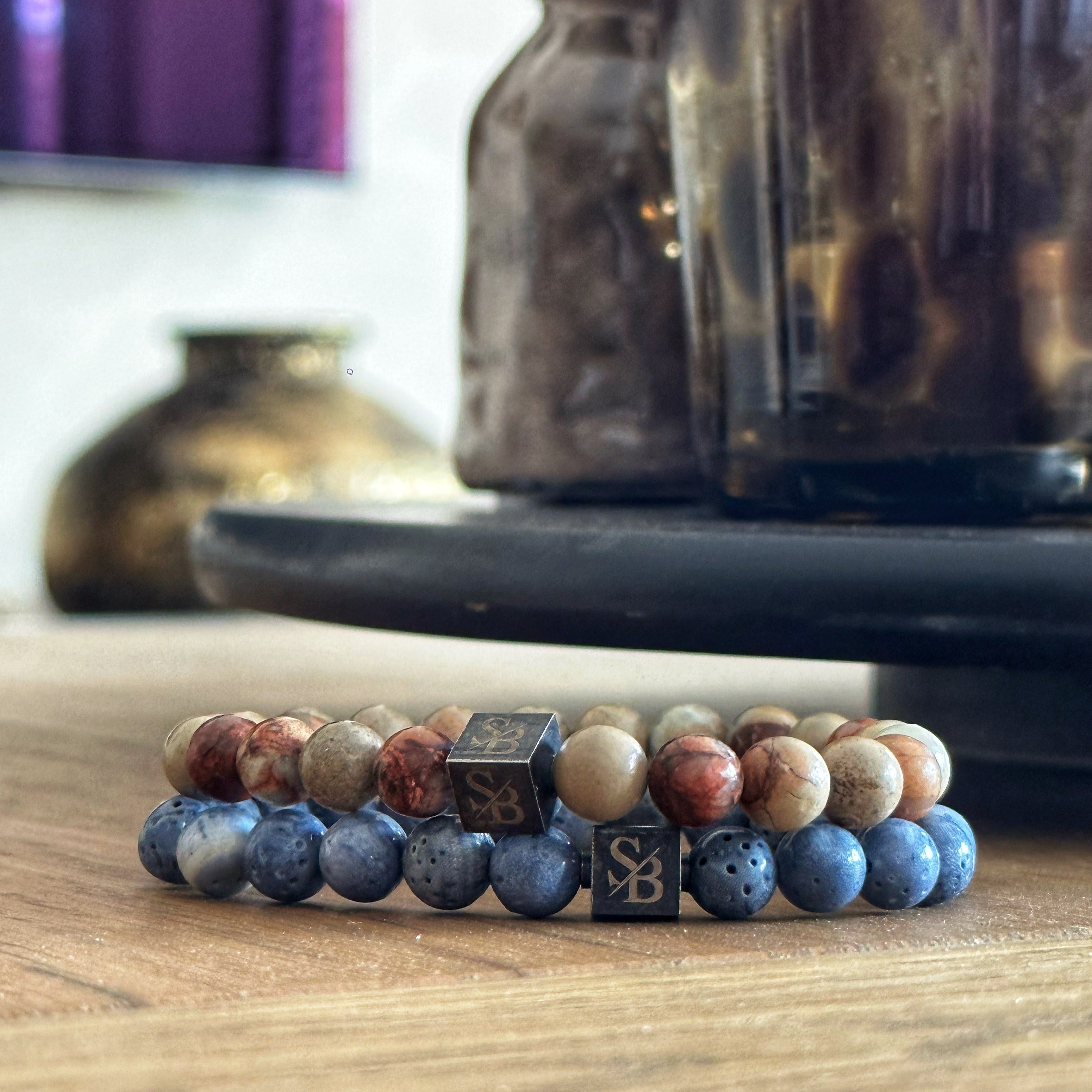 Twee Stoney-armbanden met blauwe en bruine serpentijnstenen (8 mm) op een houten tafel.