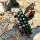 Een stapel Dragon Set-armbanden gemaakt van kralen van Stoney Bracelets, zittend op een boomstam op het strand.