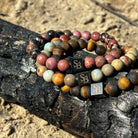 Twee Stoney Bracelets Tropical Sets (8 mm) op een boomstam in het zand.