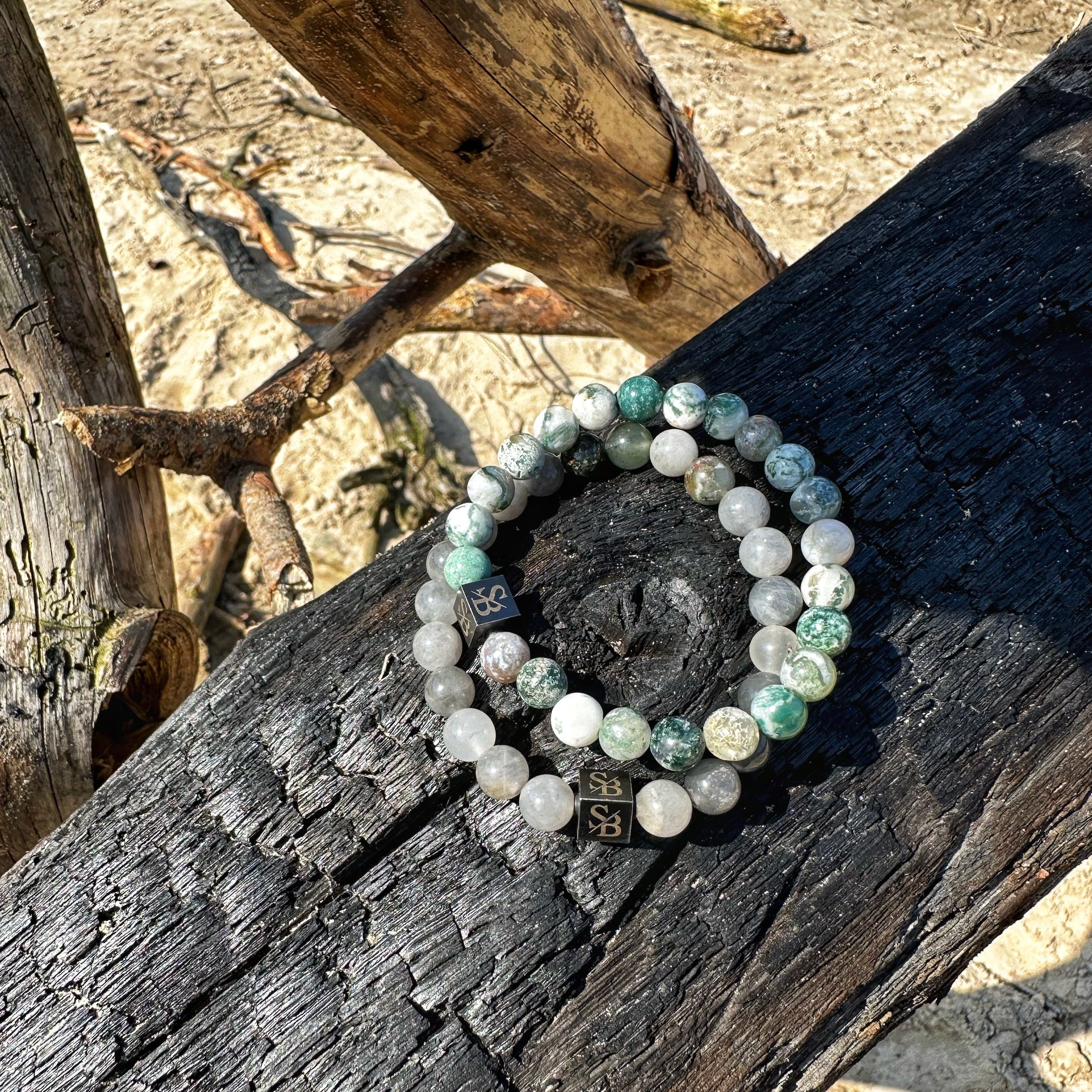 Een Elegance Set (8 mm) armband zittend op een boomstam op het strand van Stoney Bracelets.