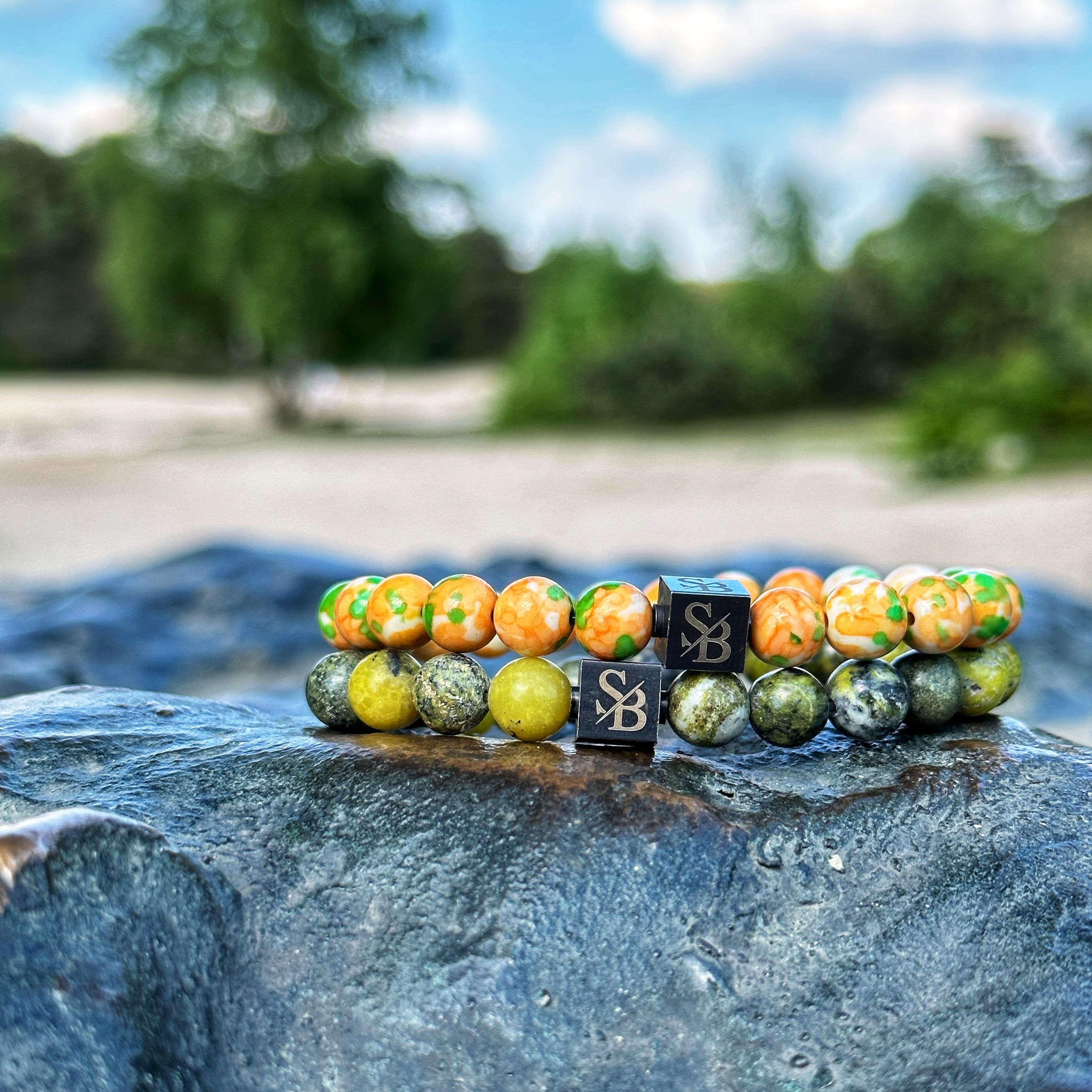 Een paar Stoney Bracelets Venom Set (8 mm) zittend op een natuursteen naast het water.