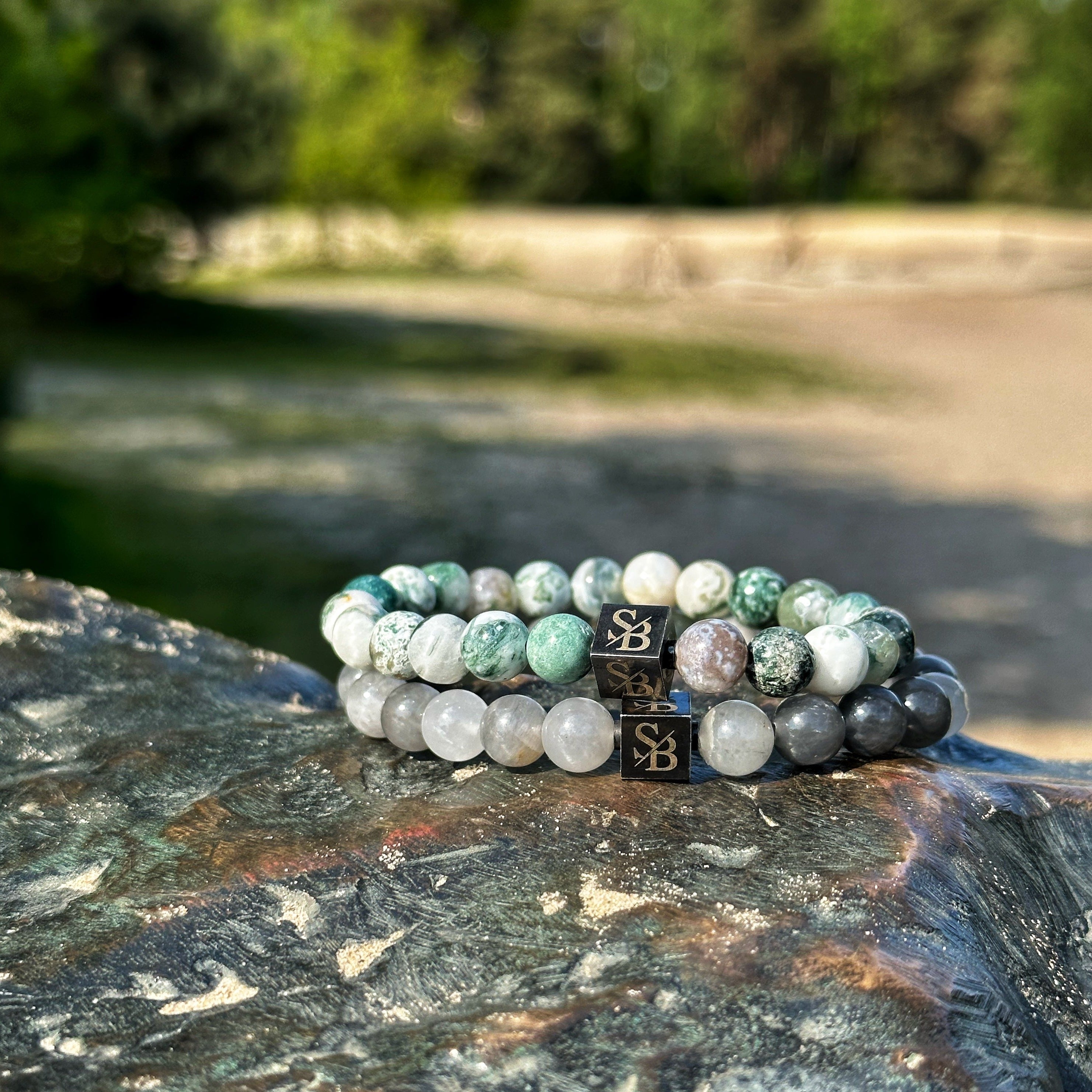 Een paar Stoney Bracelets Elegance Set (8 mm) zittend op een rots in het bos.