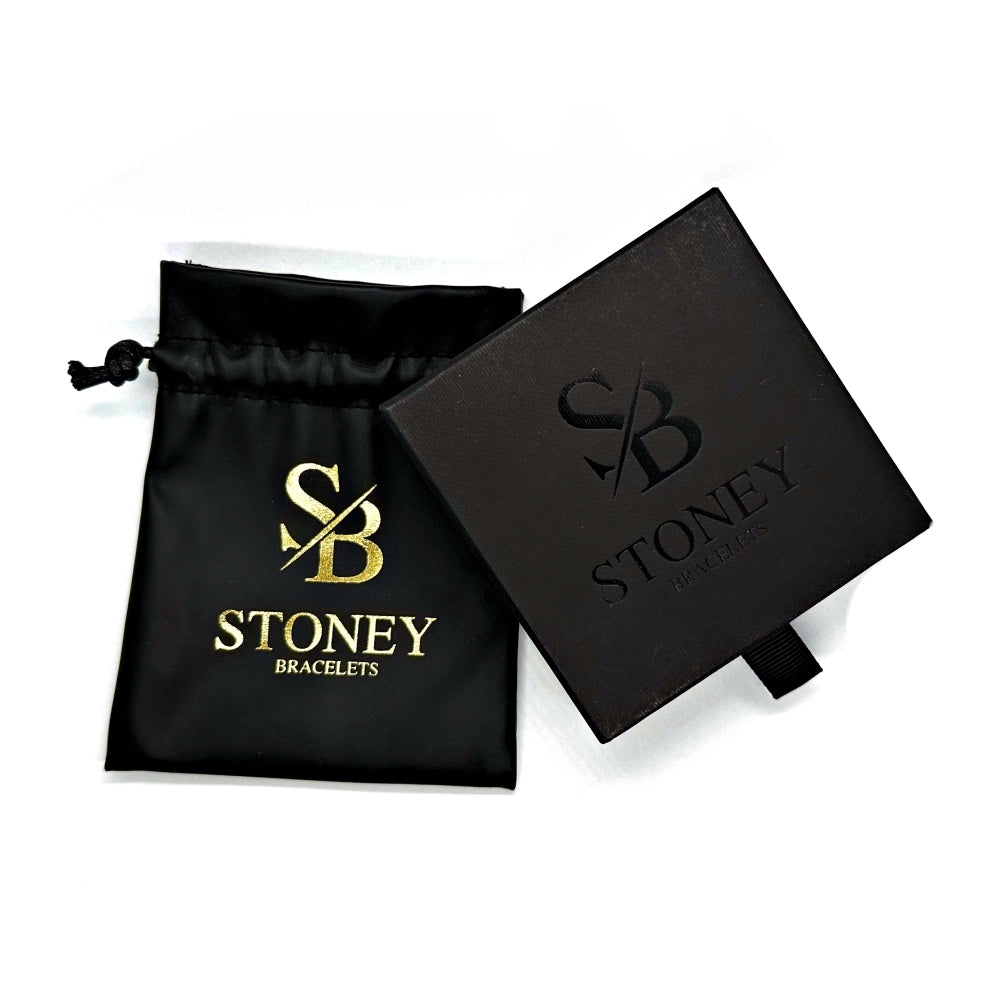 Een zwart trekkoordzakje versierd met een gouden "Stoney Bracelets"-logo is naast een gesloten zwarte doos geplaatst, die ook hetzelfde logo in reliëf op het deksel heeft. De doos, uitgerust met een klein treklipje aan één kant, dient als een elegante verpakkingsoplossing die ideaal is om uw door de natuur geïnspireerde Matte Obsidian Stones (6mm) armbandcollectie te presenteren.