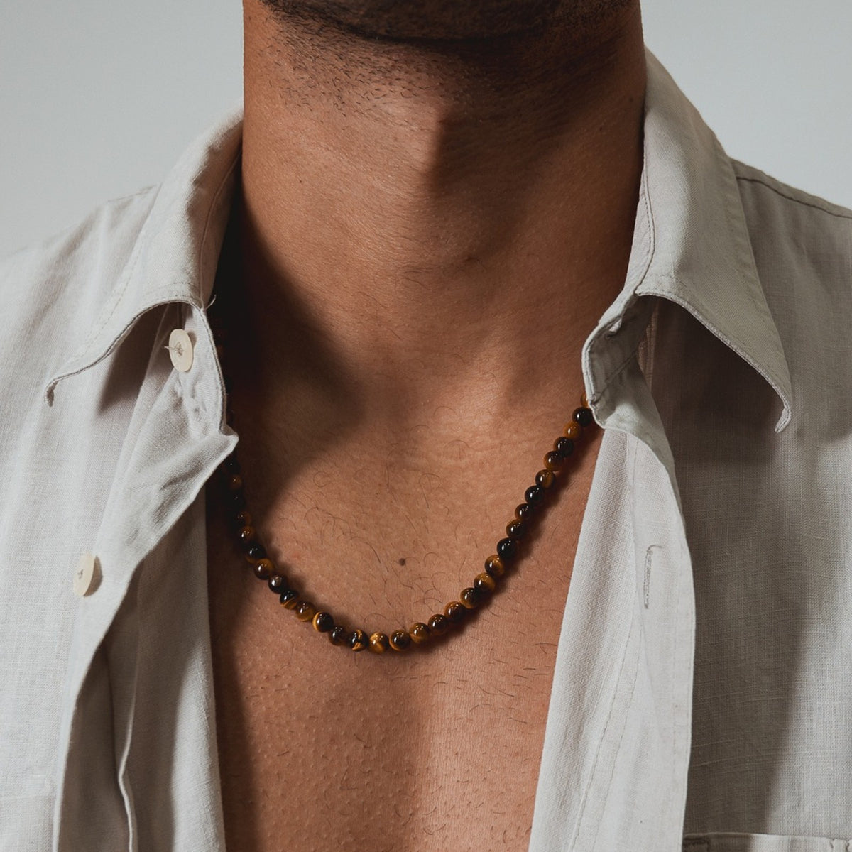 Golden Gaze Necklace (6mm) gedragen op de huid onder een open linnen overhemd, tijgeroog kralen | Stoney Bracelets