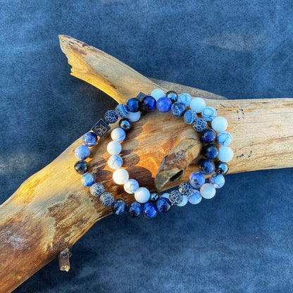 Een paar Stoney Bracelets Water Set (8mm) armbanden met blauwe en witte stenen op een stukje natuursteen.