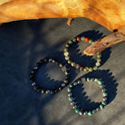 Drie Prehistorisch | Mixed Stones (8mm) natuursteen armbanden van Stoney Bracelets liggen op een boomstam op tafel.
