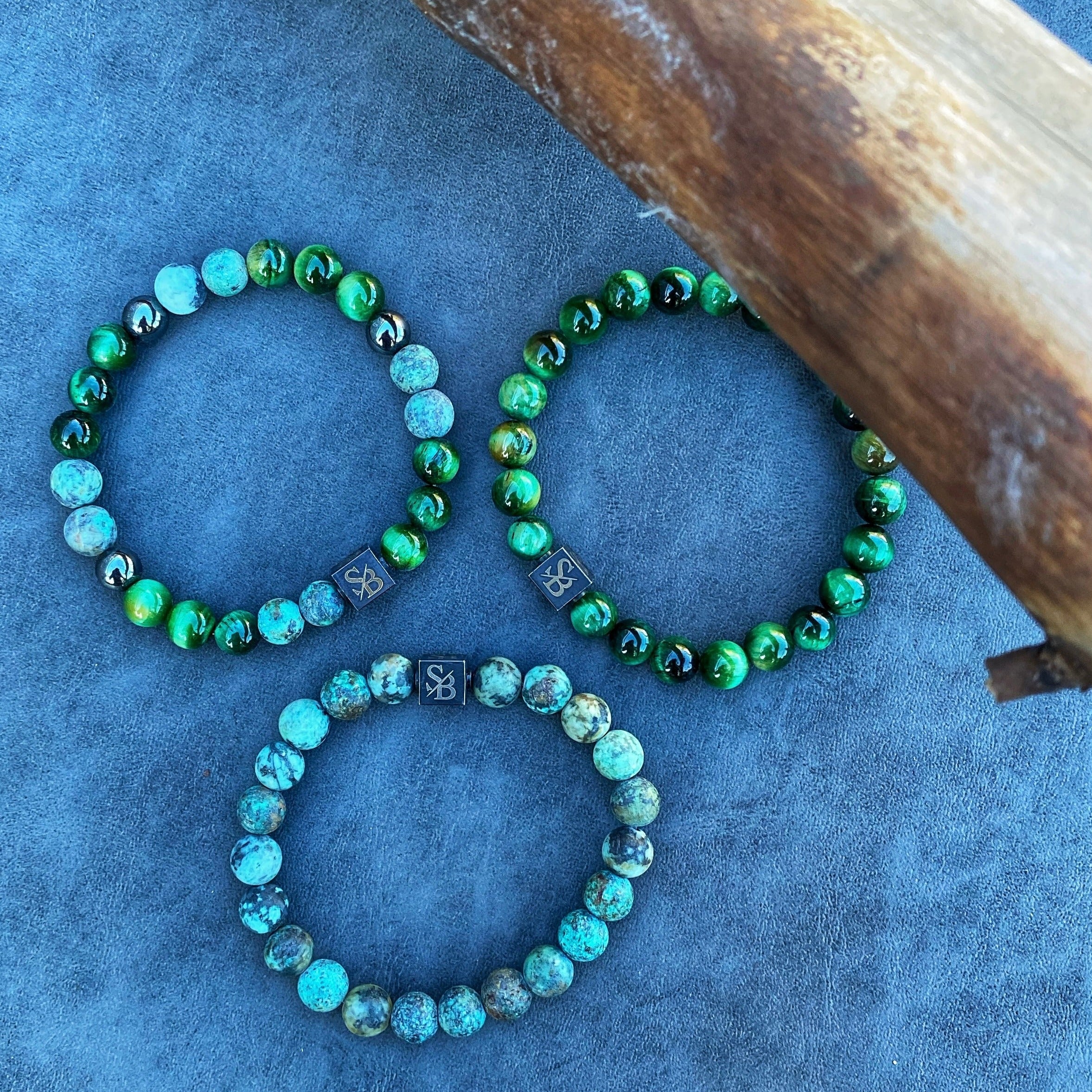 Drie armbanden met groene en zwarte Moeras | Mixed Stones (8mm) kralen bovenop een boomstam van Stoney Bracelets.