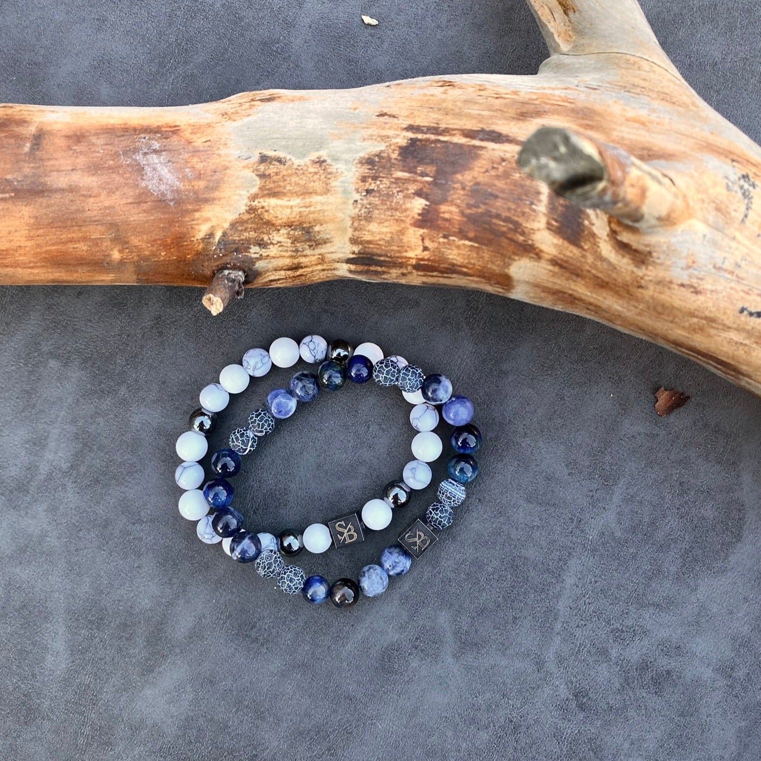 Twee Arctische | Mixed Stones (8mm) armbanden met blauwe en witte stenen bovenop een boomstam van Stoney Bracelets.