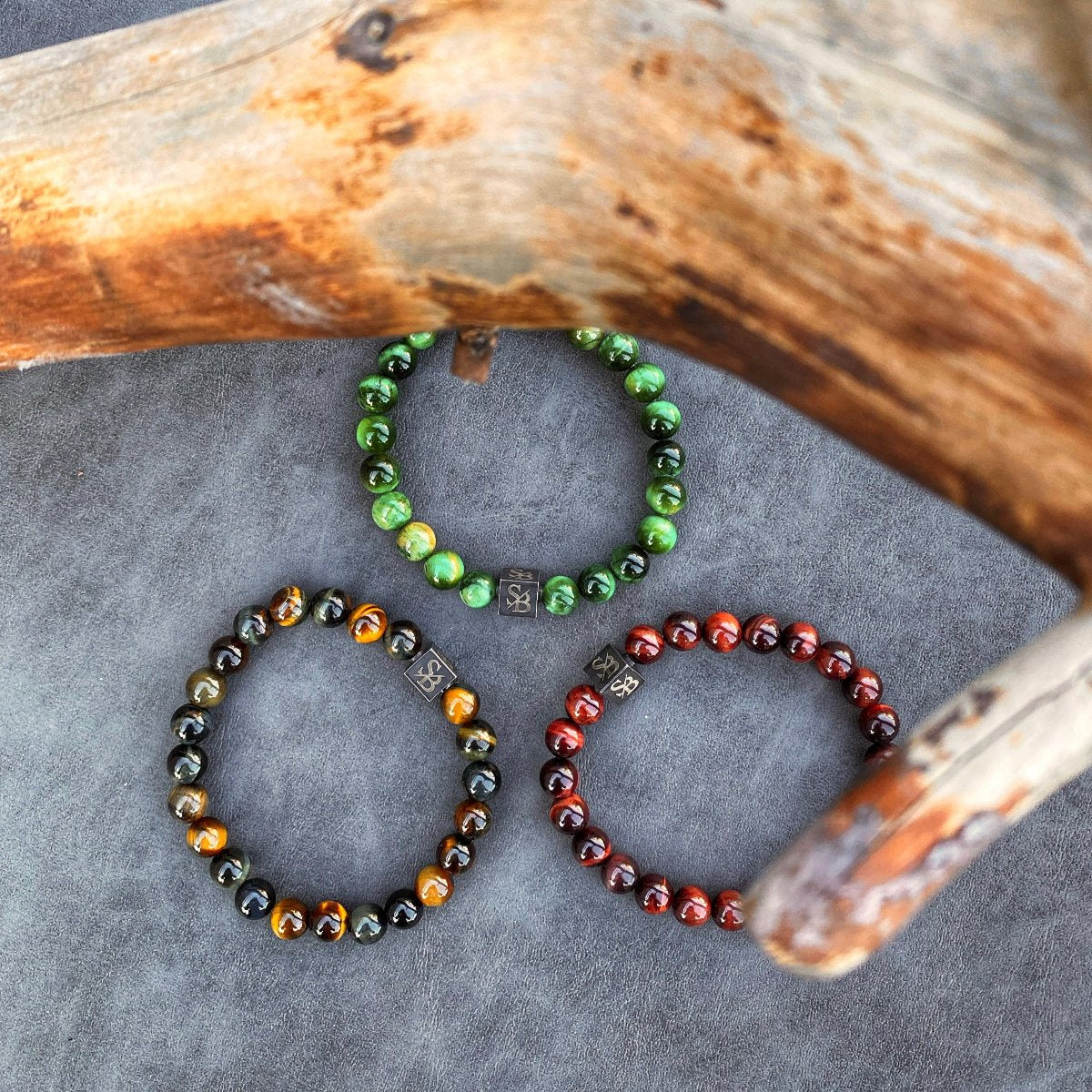 Drie Rode Tijgeroogstenen (8mm) armbanden op een stuk hout van Stoney Bracelets.