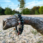 Een Stoney Bracelets Serpent Set (8 mm) armband versierd met kralen, rustend op een boomstam in het zand.