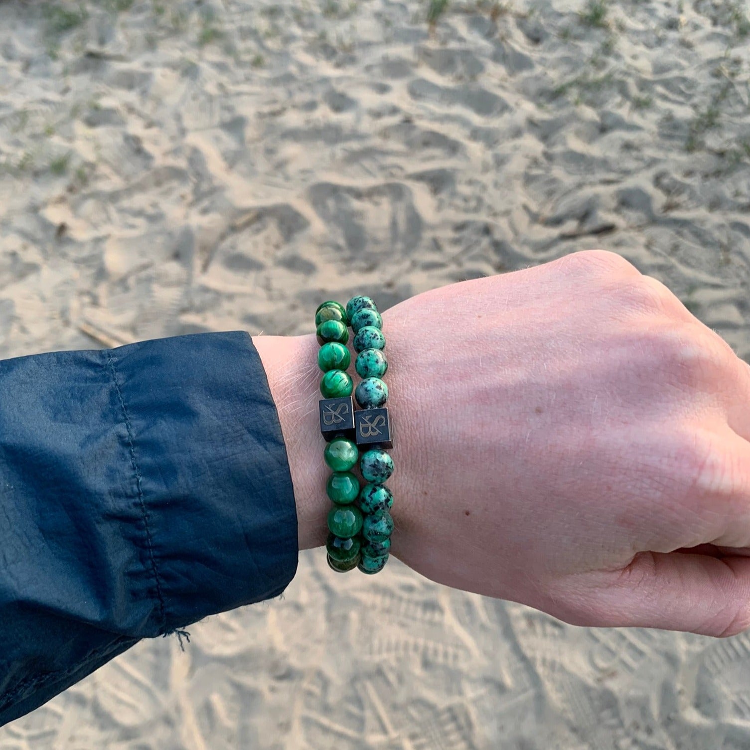 Een persoon die een groene en zwarte Stoney Bracelets Nature Set (8 mm) armband draagt op het strand.
