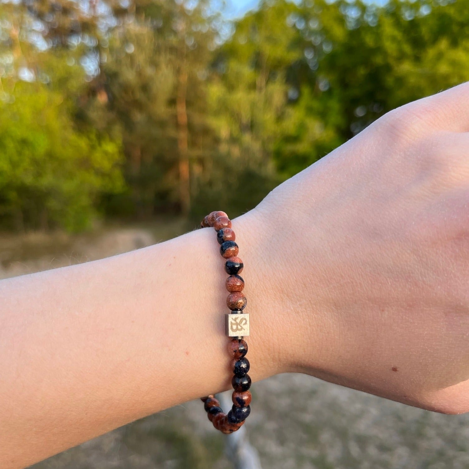 De hand van een vrouw houdt een Stoney Bracelets armband met koperen zandstenen (6 mm) gemaakt van natuursteen.
