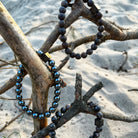 Drie Stoney Bracelets Wood Sets (8 mm) zittend op een tak op het strand.