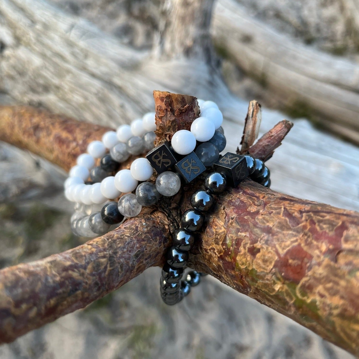 Drie Stoney Armbanden Engelenset (8 mm) kralenarmbanden liggend op een tak aan het strand.