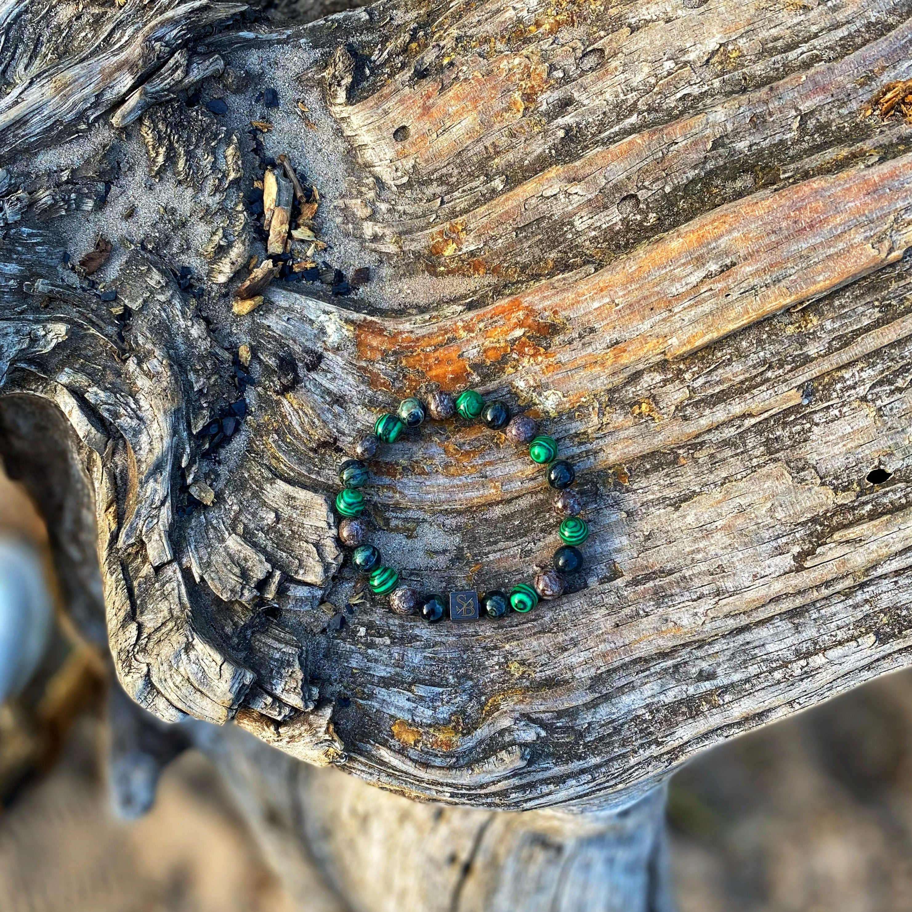 Een groene en zwarte Scandinavische | Mixed Stones (8mm) armband van Stoney Bracelets zittend op een stuk hout onder andere sieraden.