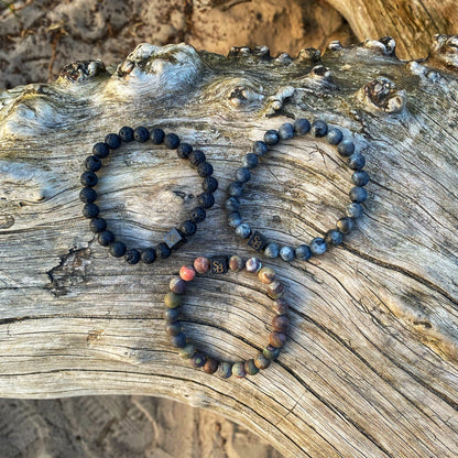 Drie Earth Set (8 mm) Stoney-armbanden rustend op een boomstam.