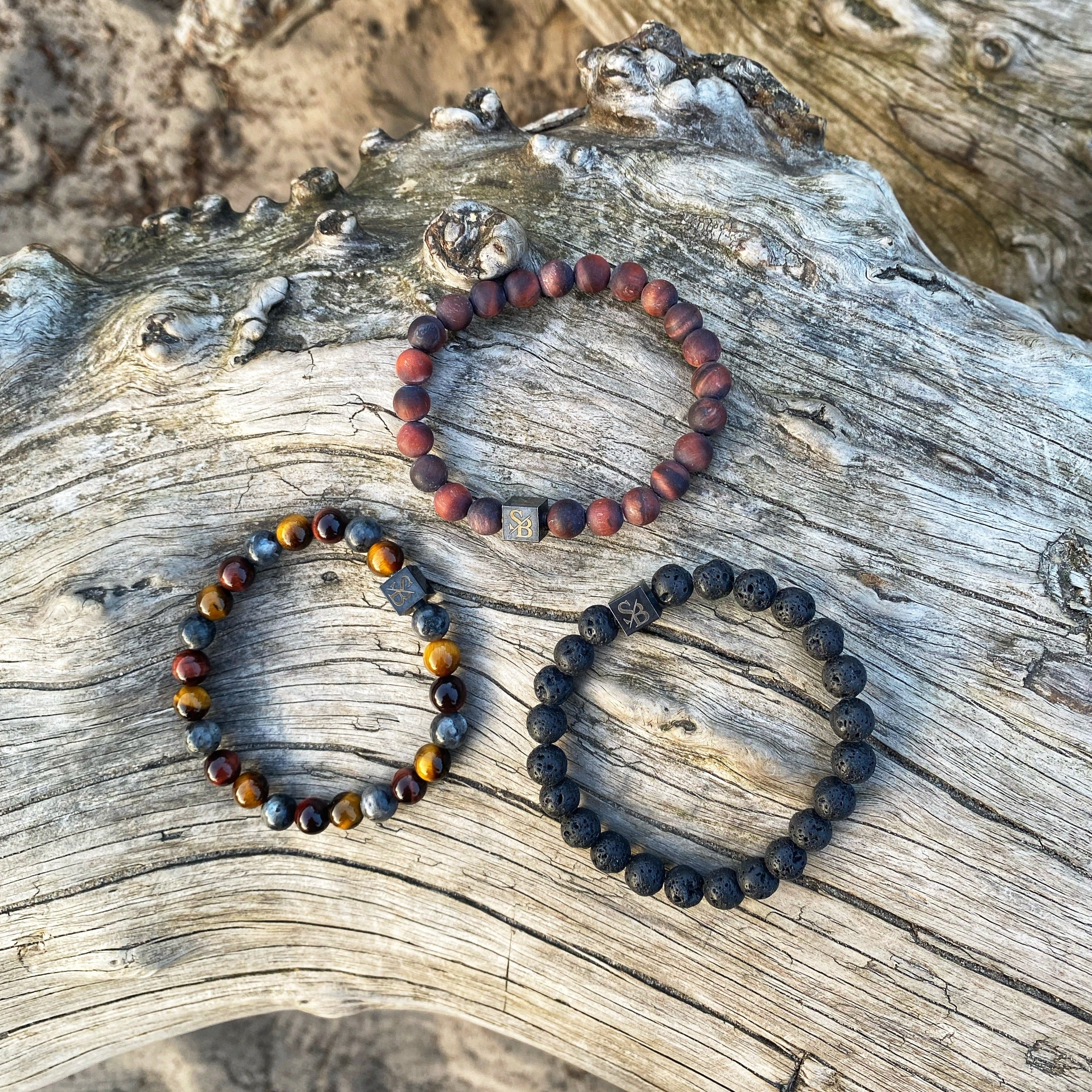 Drie Stoney Bracelets Fire Sets (8 mm) zittend op een boomstam op het strand.