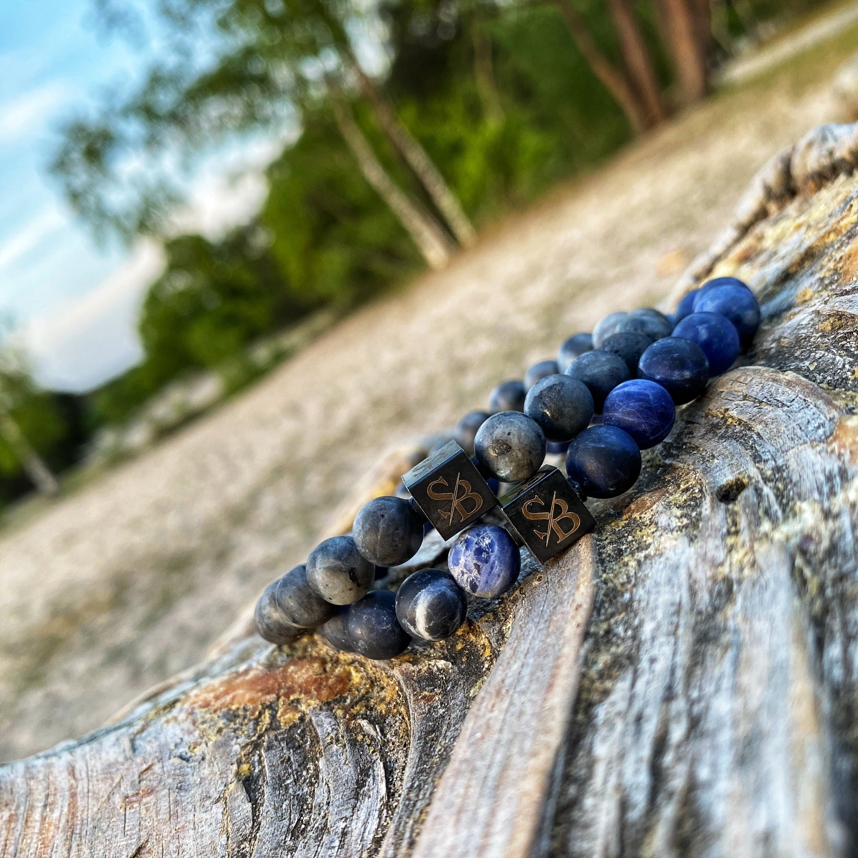 Een Stoney Bracelets Matte Lapis Lazuli Set (8mm) armband met blauwe stenen bovenop een boomstam.