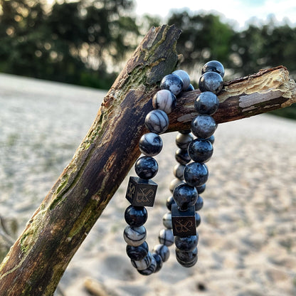 Een paar Stoney Bracelets Double Grey Set (8mm) armbanden zittend op een tak.