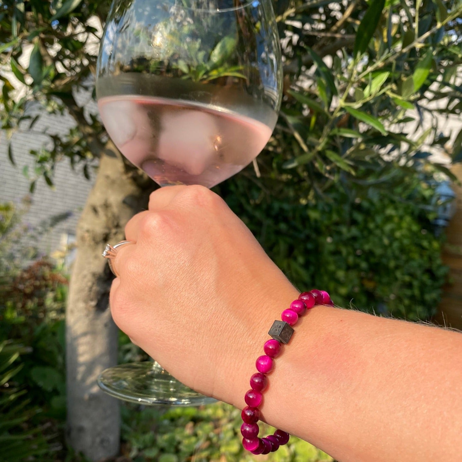 Een vrouw die een glas wijn vasthoudt met een kralenarmband van Stoney Bracelets Rose Tiger Eye Stones (6 mm).