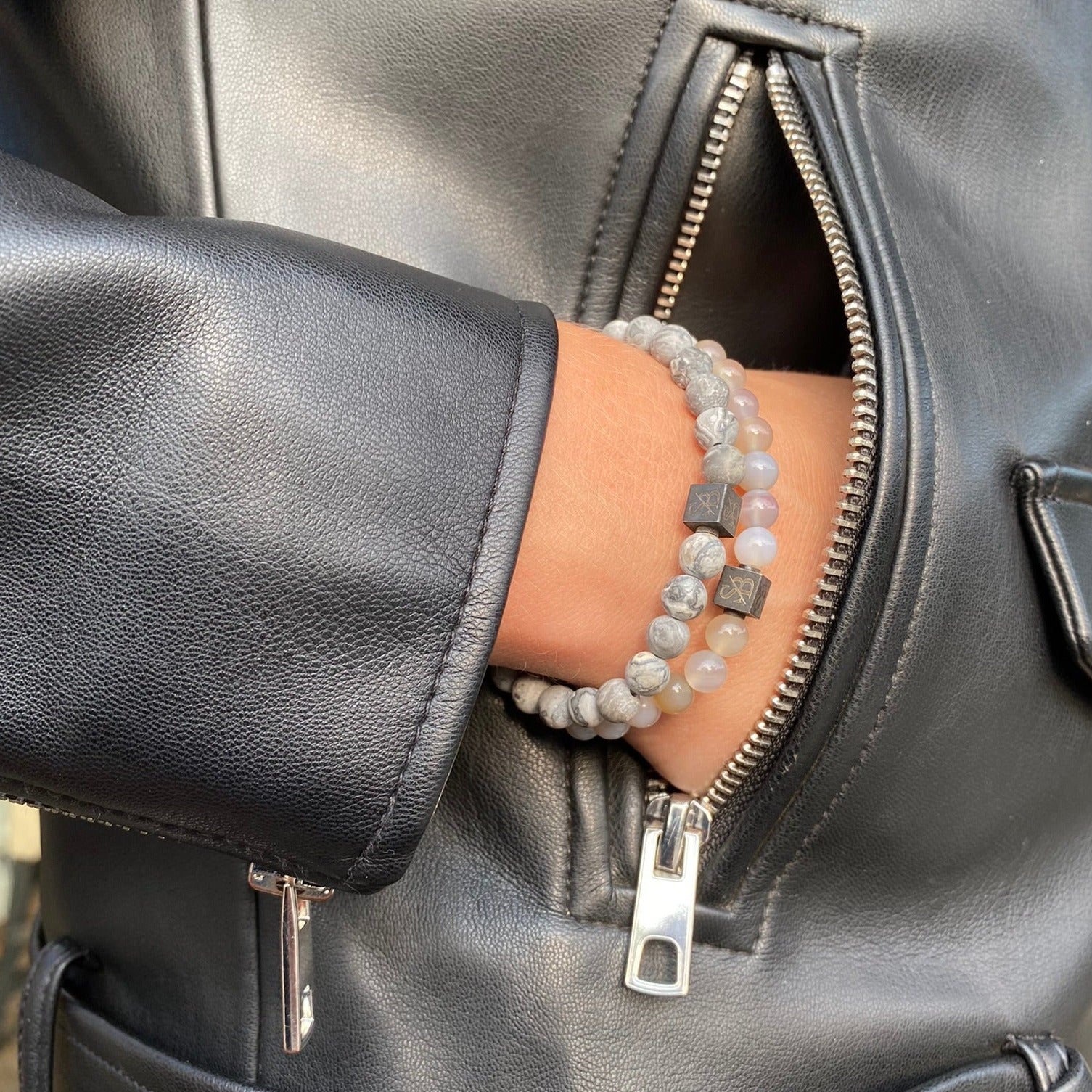 Een vrouw in een leren jasje draagt een grijze kralenarmband gemaakt van gestreepte agaatstenen (6 mm) van Stoney Bracelets.