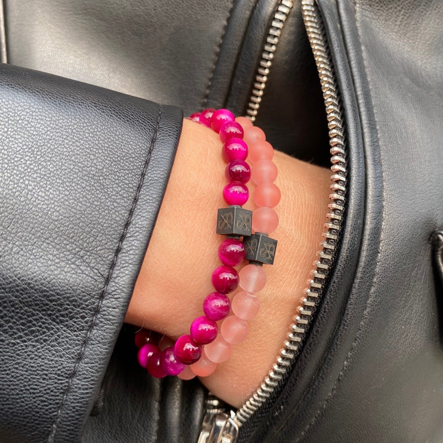 De hand van een vrouw houdt een roze en zwarte kralenarmband vast, gemaakt van Rose Tiger Eye Stones (6 mm) van Stoney Bracelets.