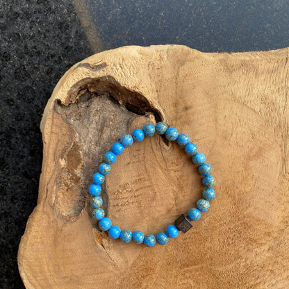 Een Stoney-armband met gouden turquoise stenen (6 mm) rustend op een stuk hout.