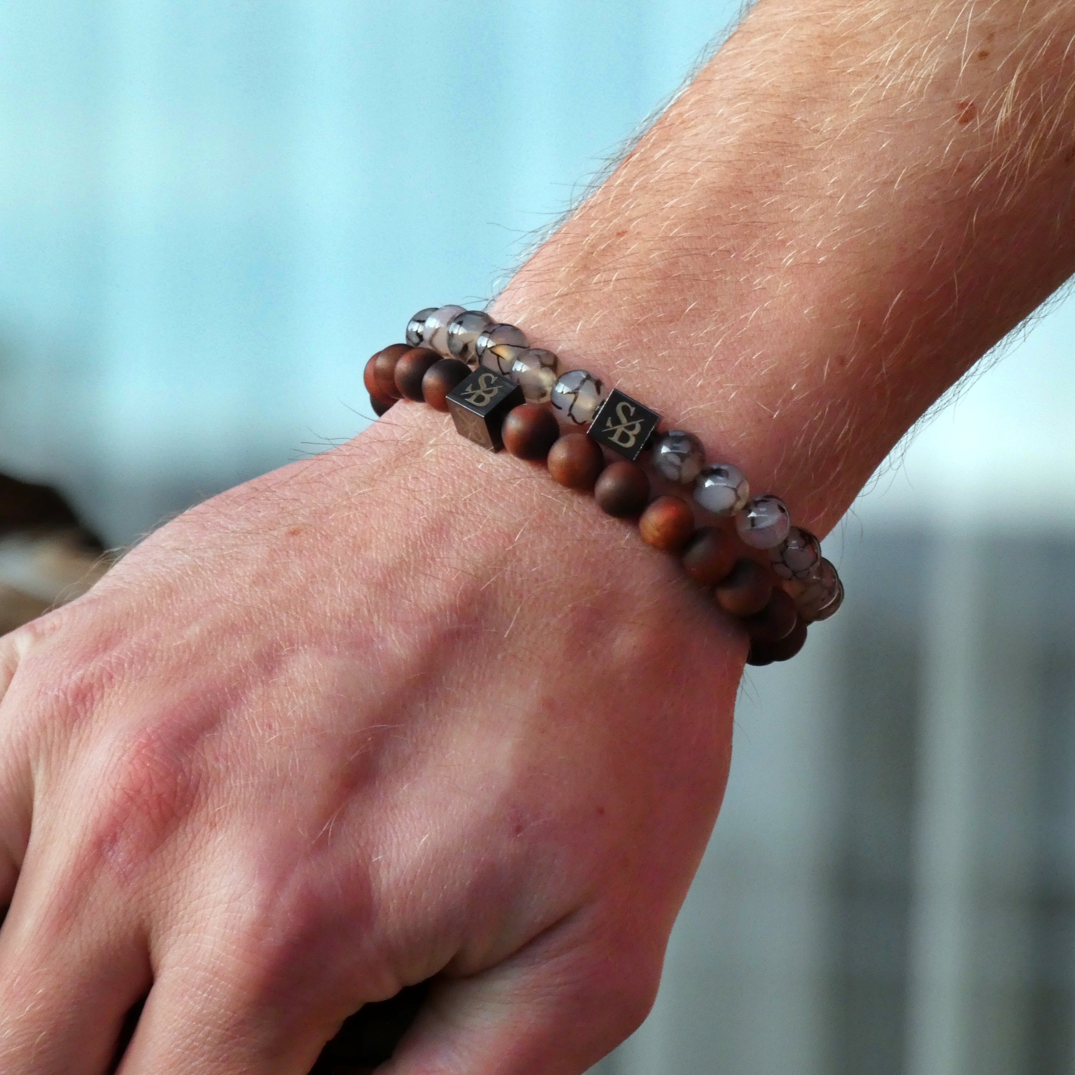 De hand van een man toont een paar houten armbanden van Stoney Bracelets Dragon Vein Stones (8 mm).
