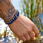 Een man met tatoeages die een Stoney Bracelets Mountain Set-armband (8 mm) vasthoudt.